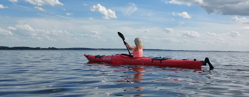 Frau paddelt in rotem Kajak auf dem See